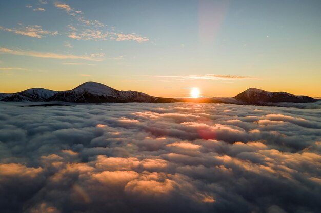 Aerial view of vibrant sunrise over white dense clouds with distant dark mountains on horizon.