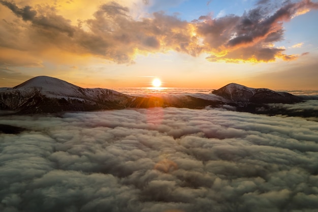 Aerial view of vibrant sunrise over white dense fog with distant dark Carpathian mountains on horizon.