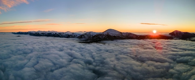 Aerial view of vibrant sunrise over white dense fog with distant dark carpathian mountains on horizon.