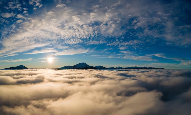 Aerial view of vibrant sunrise over white dense fog with distant dark Carpathian mountains on horizon