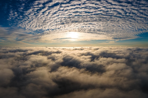 Aerial view of vibrant yellow sunrise over white dense clouds with blue sky overhead.