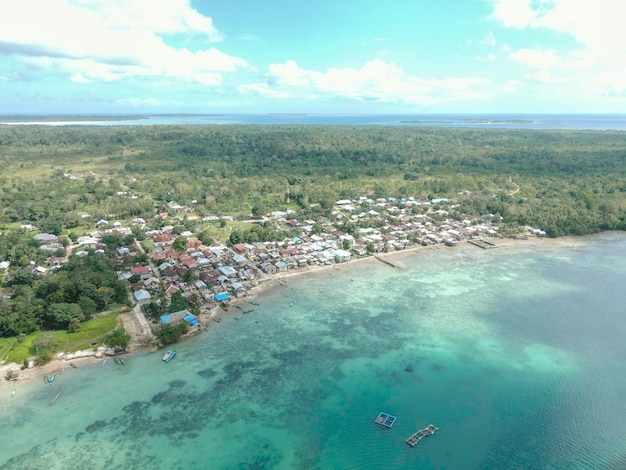 インドネシア、マルクの背景に小さな島がある美しいビーチの近くの村の空撮