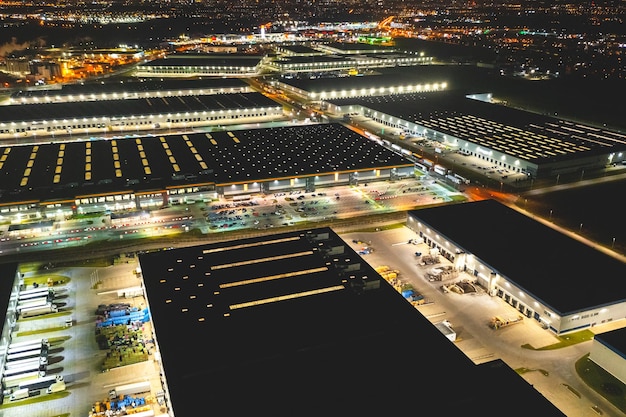 Photo aerial view of a warehouse of goods at night aerial view of industrial area logistics warehouses and many trucks at night