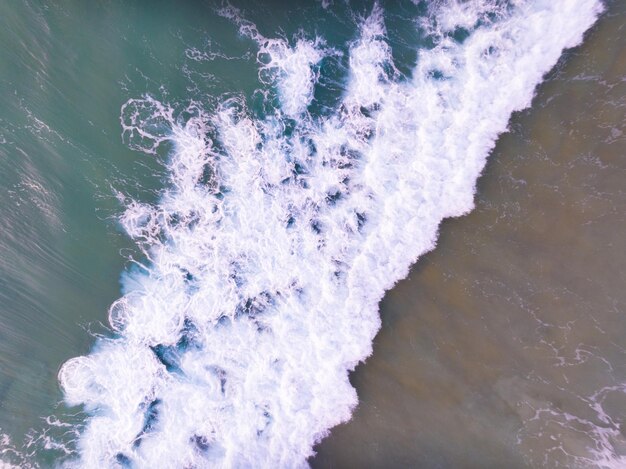 Aerial view of Waves crashing on sandy shoreSea surface ocean waves backgroundTop view beach background