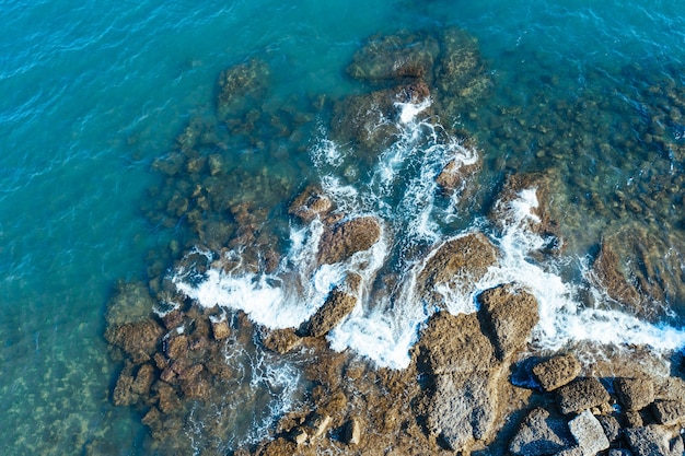 航空写真。トルコの地中海の波が岩に打ち寄せます。ターコイズブルーの海の波が高所で撃たれる