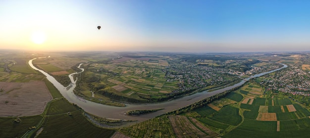 Aerial view of wide river flowing quietly in rural countryside between green fields in summer evening