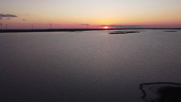 Aerial view of wind turbines and agriculture field near the sea at sunset