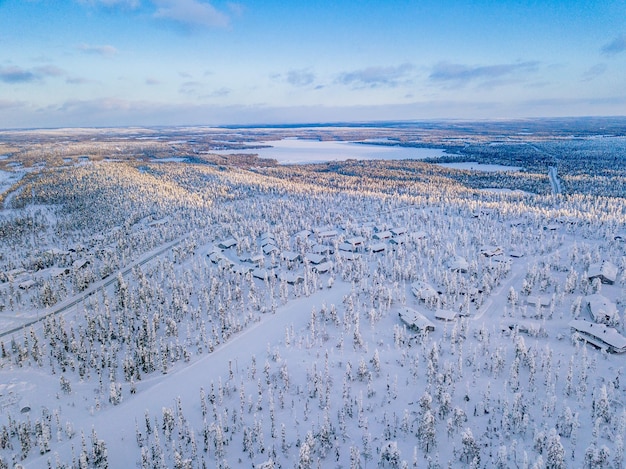 Вид с воздуха на зимний лес с морозными деревьями, сельскую дорогу и деревню в Финляндии, Лапландии