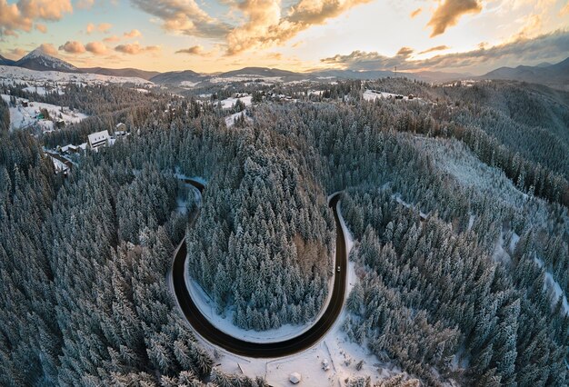 Aerial view of winter landscape with snow covered mountain hills and winding forest road in morning.