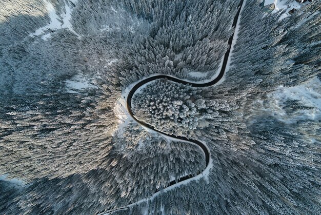 Aerial view of winter landscape with snow covered mountain hills and winding forest road in morning.