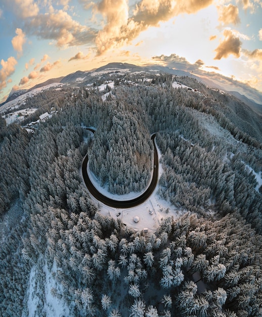 雪に覆われた山の丘と朝の曲がりくねった林道と冬の風景の空撮。