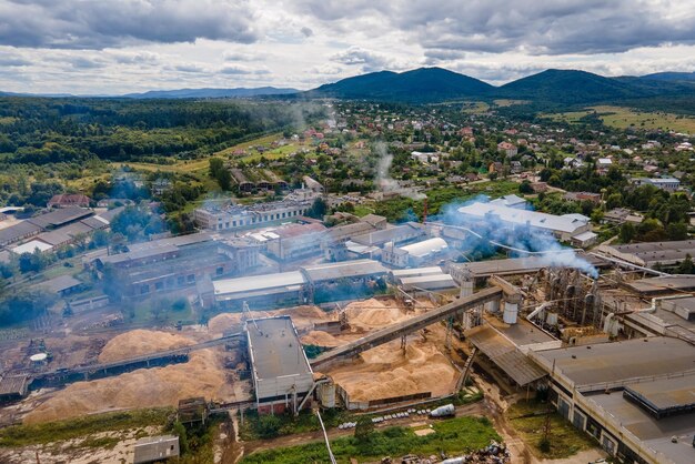 Вид с воздуха на деревообрабатывающий завод с дымовой трубой от производственного процесса, загрязняющего окружающую среду на заводе