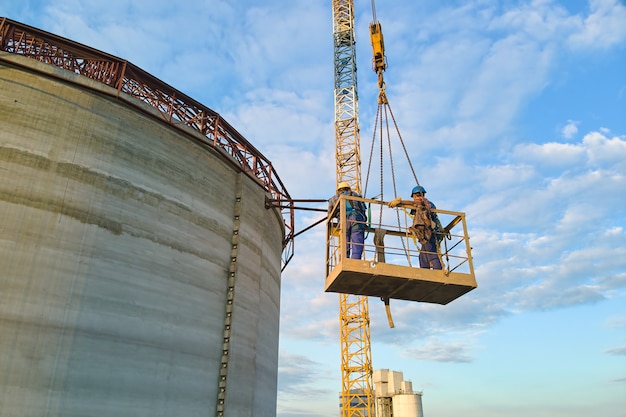 Aerial view of workers on cement factory under construction with high concrete plant structure and tower cranes at industrial production area.