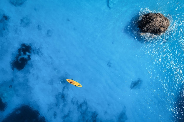 Aerial view of yellow kayak in blue sea at sunset in summer Man on floating canoe in clear azure water rocks stones Lefkada island Greece Tropical landscape Sup board Active travel Top view