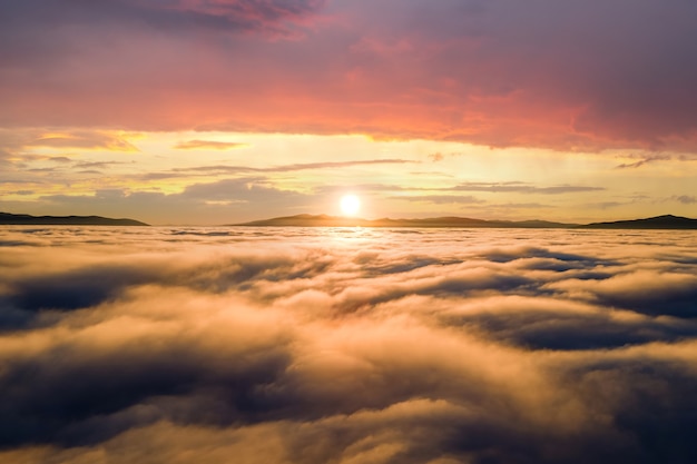 Aerial view of yellow sunset over white puffy clouds with distant mountains on horizon.