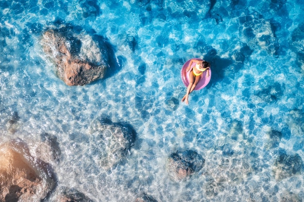 Aerial view of a young woman swimming with pink swim ring in adriatic sea at sunset in summer Landscape with girl clear blue water stones sandy beach Top view Vacation in Lefkada island Greece