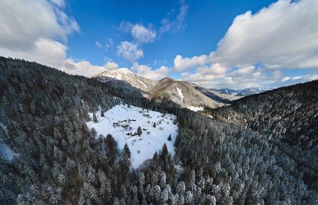 Воздушный зимний пейзаж с небольшими сельскими домиками между заснеженным лесом в холодных горах.