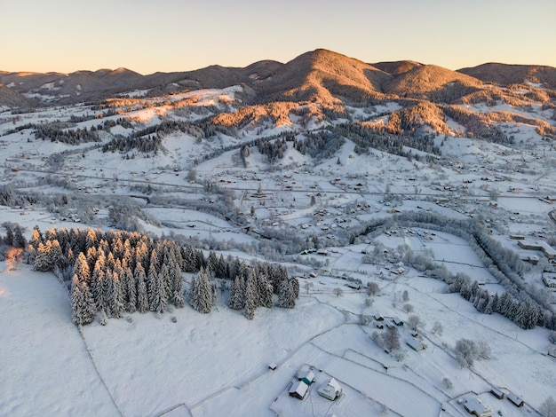 寒い山の雪に覆われた森の間に小さな村の家と空中冬の風景