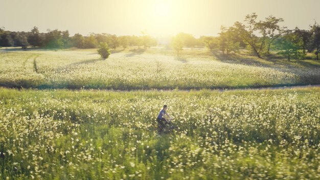 Foto aerial di una giovane donna in bicicletta su una strada di terra sun fiori verdi prato paesaggio naturale estivo