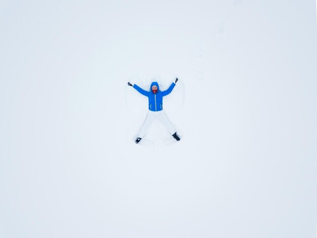 雪の天使を作り、雪で遊ぶ女性のドローンからの空中写真