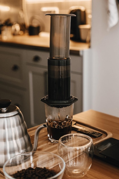 Aeropress and glass cup scales manual grinder coffee beans kettle on wooden table Professional barista preparing coffee by aeropress alternative method brewing process