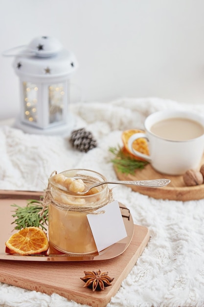 Aesthetic christmas breakfast homemade hazelnut salted caramel\
spread in glass jar with mockup label at cozy home with cup of\
coffee