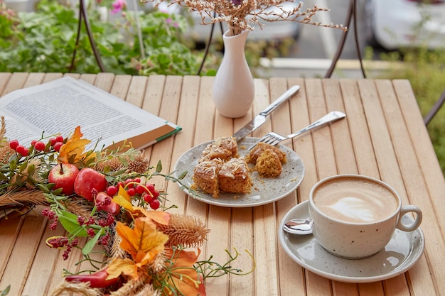 Aesthetic coffee time outside with a book cutting doughnut and
cappuccino among fall decorations on wooden table atmospheric
coffee time