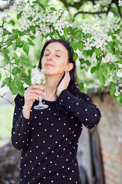 La ragazza estetica tiene un bicchiere pieno di fiori praticando la meditazione di respirazione spirituale all'esterno collegandosi con la natura vibrazioni primaverili dell'albero in fiore