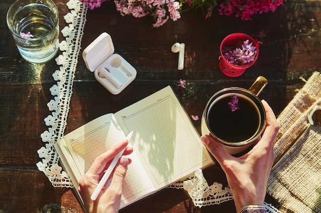 Foto cuffie wireless stile di vita estetico decorazioni di fiori lilla e tazza di caffè ascolto di musica o audiolibri, webinar o chat online, parlando al telefono in giardino mockup di blocco note