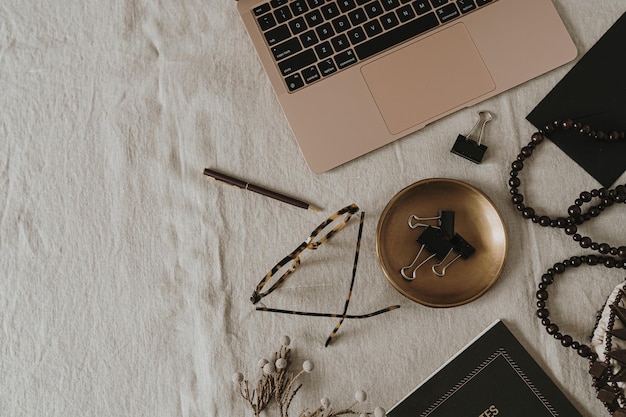 Foto composizione estetica del marchio della boutique di moda di lusso elegante area di lavoro da donna boho lady boss con computer portatile e cancelleria su biancheria di mussola beige neutra vista dall'alto piatta