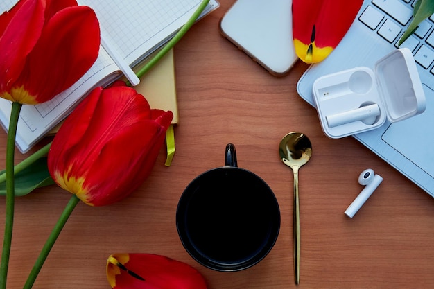 Aesthetic online work place work with red tulips and cup of coffee Online work listening to music by headphones taking webinar learn language in app online meeting learning at home office