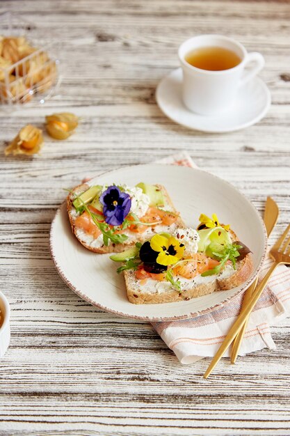 Aesthetic pescetarian breakfast sandwiches with salted salmon edible flowers avocado and cucumber Tea cup and winter cherry Atmospheric autumn lunch