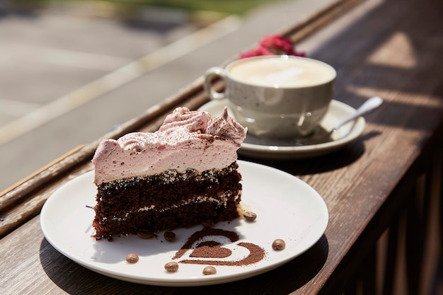 Aesthetic piece of cake,glass of cappuccino on wooden table outdoor in the cafe terrace,Hard shadows