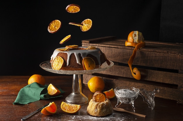 Aesthetic vibrant shot of orange slices falling on a cake covered by sweet sugar icing