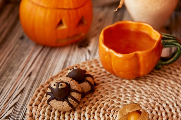 Aesthetics autumn decorations with Halloween spider cookies and cup of tea in shape of pumpkin Jack o lantern