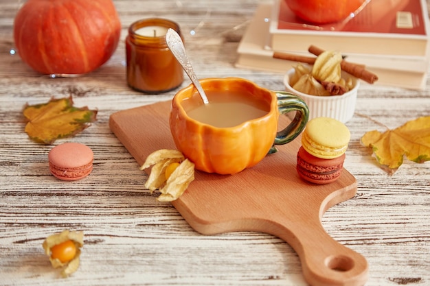 Aesthetics pumpkin latte in pumpkin cup Seasonal breakfast with coffee and macaroons among pumpkins and winter cherry Cozy autumn home