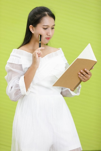 Afbeelding is portret. Aziatische glimlachende mollige vrouw die witte kleding draagt. Lady Azië staat en houdt vast en kijkt op notebook op groene achtergrond.