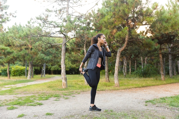 Afbeelding van Afro-Amerikaanse vrouw 20s dragen zwarte trainingspak sporten, en haar lichaam uitrekken in groen park