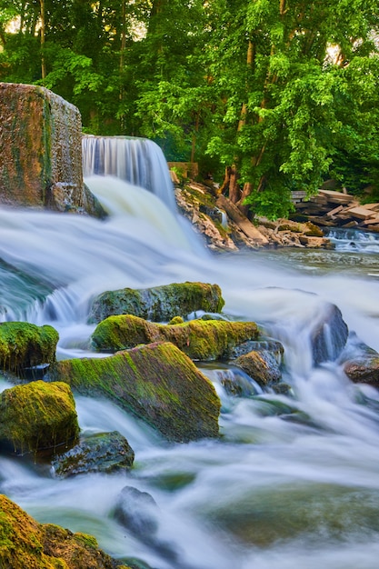 Foto afbeelding van algen die kleine rotsen bedekken die uit de rivier steken naast watervallen en stenen dam