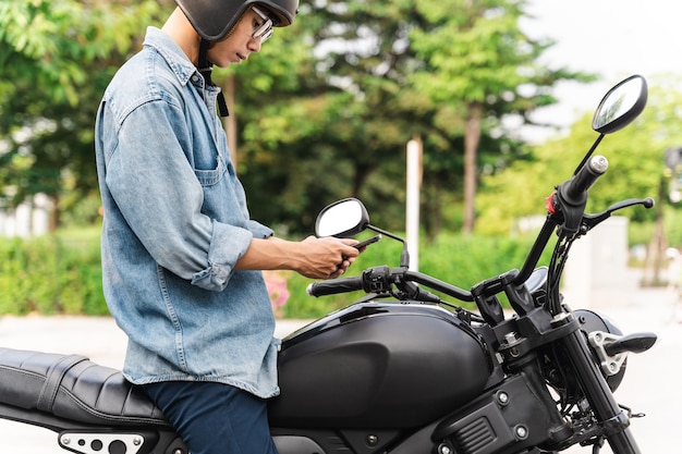 Afbeelding van aziatische man zittend op moto met mobiele telefoon