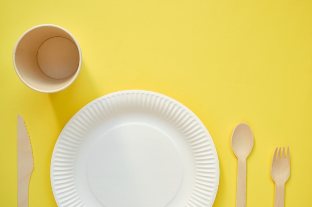 Afbeelding van bovenaf van een witte kartonnen plaat met een houten lepel aan de rechterkant en een bruin kartonnen glas aan de linkerkant op een gele achtergrond