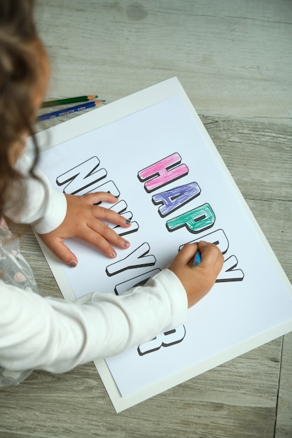 Foto afbeelding van bovenaf van onherkenbaar meisje dat gelukkig nieuwjaar belettering kleurt met kleurpotloden