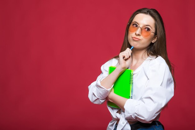 Afbeelding van denken, dromen, nadenkende jonge vrouw geïsoleerd over rode muur achtergrond schrijven van notities