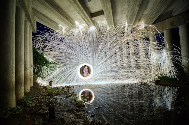 Afbeelding van Douche van witte staalwolvonken en een cirkelvormig portaal met een man aan de andere kant en allemaal onder een betonnen brug