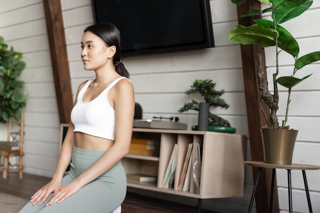 Afbeelding van een aziatische vrouw die zich concentreert tijdens ochtendmeditatie, oefen yoga thuis, zittend in...