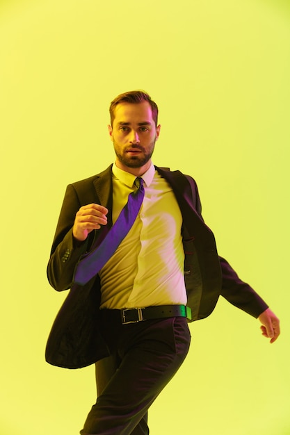 Afbeelding van een blanke serieuze zakenman in een formeel pak die gebaren maakt tijdens het lopen geïsoleerd over een gele muur