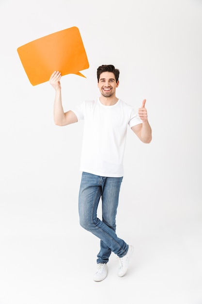 Afbeelding van een emotionele opgewonden jongeman die zich voordeed geïsoleerd over een witte muur met een tekstballon die duimen omhoog laat zien.