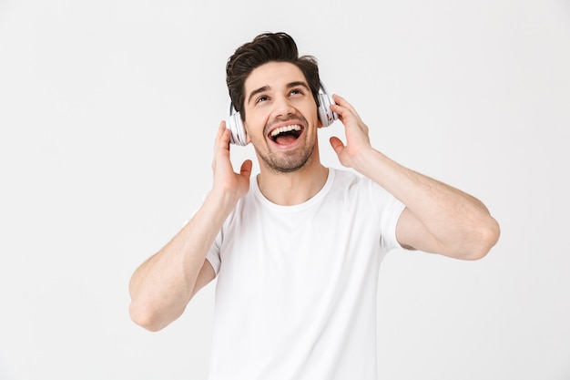 Afbeelding van een emotionele opgewonden jongeman die zich voordeed over een witte muur die muziek luistert met een koptelefoon.