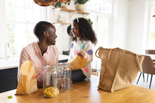 Afbeelding van een gelukkige Afro-Amerikaanse moeder en dochter die boodschappentassen uitpakken in de keuken