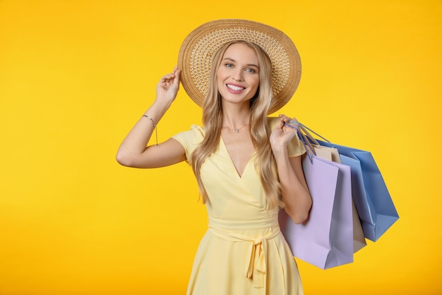 Afbeelding van een gelukkige jonge vrouw met een hoed die geïsoleerd staat over een gele achtergrond met boodschappentassen